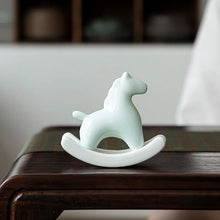 Load image into Gallery viewer, This Petite Ceramic Rocking Horse by Allthingscurated is a work of art. Crafted by hand from ceramic and decorated with a beautiful crackle pattern, it exudes a subtle far-eastern beauty and grace. Makes a perfect gift for those who appreciate quality craftsmanship and a treasured gift to any horse collector. Comes in green and azurerish white. Measures 9.8cm or 3.8 inches in height, 10.4cm or 4 inches in width and 4.2cm or 1.6 inches in depth. Featured here is an Azurerish White horse.