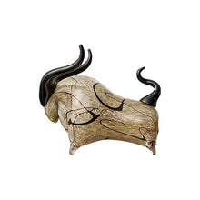 Load image into Gallery viewer, Decorative bull sculptures on books with a candle against a textured white wall. Rex Decorative Bull by Allthingscurated are meticulously handmade from high quality glass. Comes in three striking finishes—an all-all black edition or two-tone variants featuring bold graphic elements. Rex brings contemporary flair and bold energy to any room. More than décor, it’s an ideal gift for those born under the Ox zodiac and Taurus sign. Shown here is the beige black bull.
