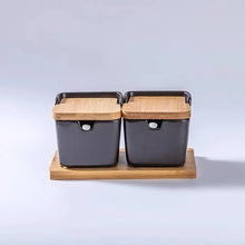 Load image into Gallery viewer, Ceramic Seasoning Storage Jars by Allthingscurated are the perfect storage solution to keep your herbs, seasonings and spices. Made of durable ceramic with a sustainable bamboo flip lid for easy access during cooking. These jars are not only functional but also environmentally friendly. Comes with a bamboo tray and ceramic spoons. Featured here is a set of 2 black jars with spoons and tray.