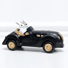 Load image into Gallery viewer, Our Regal Rabbit Family Figurines by Allthingscurated are beautifully-crafted and decorative. Made high-quality resin, these unique figurines will add a touch of elegance and whimsy to your home décor. Available in 6 designs, they are the perfect additions to your spring and Easter decorations. Featured here is Car Riding Rabbits.