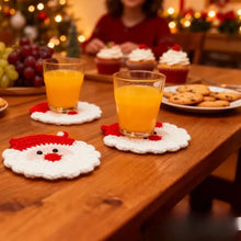 Load image into Gallery viewer, Red and white Santa Claus design crochet coasters with two glasses of orange juice, cookies and cupcakes on a wooden table.