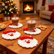 Load image into Gallery viewer, Red and white Santa Claus design crochet coasters with hot chocolate drink laid on a wooden table, with some cookies, shot in a living room setting with a lighted Christmas and fireplace in the background.