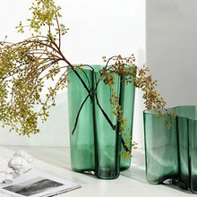 Load image into Gallery viewer, Green glass vases with branches on a white surface. The Dayton Vase by Allthingscurated offers a beautiful asymmetrical design that feels both timeless and organic. Its sculptural, minimalist form brings a striking yet harmonious touch to any home interior. Available in clear, green and amber, it’s an unforgettable gift for housewarmings, weddings or holidays.