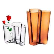 Load image into Gallery viewer, Two glass vases, one clear and one amber with red roses on a white background. The Dayton Vase by Allthingscurated offers a beautiful asymmetrical design that feels both timeless and organic. Its sculptural, minimalist form brings a striking yet harmonious touch to any home interior. Available in clear, green and amber, it’s an unforgettable gift for housewarmings, weddings or holidays.
