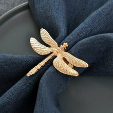 Load image into Gallery viewer, Dragonfly Napkin Rings by Allthingscurated come as a set of 6 rings in either classic gold or perennial green design. These dragon-shaped rings featured vivid venation patterns on their wings, adding a touch of natural beauty to any botanical-themed setting. Perfect for elevating your Summer tablescape. Featured here is the gold design.
