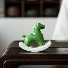 Load image into Gallery viewer, This Petite Ceramic Rocking Horse by Allthingscurated is a work of art. Crafted by hand from ceramic and decorated with a beautiful crackle pattern, it exudes a subtle far-eastern beauty and grace. Makes a perfect gift for those who appreciate quality craftsmanship and a treasured gift to any horse collector. Comes in green and azurerish white. Measures 9.8cm or 3.8 inches in height, 10.4cm or 4 inches in width and 4.2cm or 1.6 inches in depth. Featured here is a Green horse.