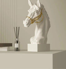 Load image into Gallery viewer, White horse head sculpture with gold bridle on a beige shelf with a diffuser bottle. Fargo Horse Head Bust by Allthingscurated is an elegant decorative sculpture with meticulous detail and flaunts a gorgeous gold-accented bridle. Perfect for horse enthusiasts and makes a meaningful gift for those born under the Horse zodiac sign. And expertly crafted to complement both timeless classic and contemporary modern interiors.