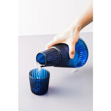 Load image into Gallery viewer, Hanis Fluted Bedside Water Carafe by Allthingscurated has a generous capacity of 1000 ml or 33.8 fluid ounce. Its minimalist design boats a fluted body and distinctive conical shape, making it a stylish drinkware that is also a beautiful home décor piece. Crafted from durable, heat-resistant glass for long-lasting use. Choose from 4 stunning colors in Amber, Blue, Green and Black. Each carafe comes with matching cover that doubles as a drinking cup.