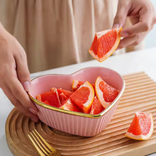 Load image into Gallery viewer, Heart-shaped pink bowl with sliced grapefruits on a wooden surface. Gold-rimmed Heart Shape Ceramic Bowl by Allthingscurated is a beautiful and versatile piece to own in your dinnerware collection. Perfect for salads, desserts and appetizers, its charming design adds an extra touch of romance for Valentine’s Day dinner; and make everyday meals extra special.