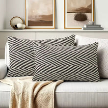 Load image into Gallery viewer, Herringbone pattern lumbar pillows on a sofa with decorative elements in the background by Allthingscurated.