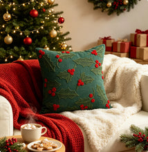 Load image into Gallery viewer, Green throw pillow embroidered with holly leaves and red berries, resting on a white sofa with a red knit blanket for festive home decor.