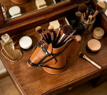 Load image into Gallery viewer, A top down view of a brown faux leather horse-head shaped holder with cosmetic brushes sitting on a wooden vanity table with mirror. Styled props include perfume bottle, makeup items in a softly lit indoor setting.