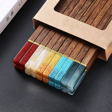 Load image into Gallery viewer, Set of colorful chopsticks with a brown box on a dark surface. Faux Jade Wooden Chopsticks by Allthingscurated feature five striking colors with jade embellishment crafted from high-grade resin that is contemporary in design yet practical in everyday dining or special occasions. Come as a set of 5 pairs or 10 pairs.