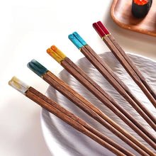 Load image into Gallery viewer, Set of wooden chopsticks with colorful tips on a white plate. Faux Jade Wooden Chopsticks by Allthingscurated feature five striking colors with jade embellishment crafted from high-grade resin that is contemporary in design yet practical in everyday dining or special occasions. Come as a set of 5 pairs or 10 pairs.
