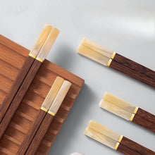 Load image into Gallery viewer, Wooden chopsticks with gold accents and ivory tip on a wooden tray against a light gray background. Faux Jade Wooden Chopsticks by Allthingscurated feature five striking colors with jade embellishment crafted from high-grade resin that is contemporary in design yet practical in everyday dining or special occasions. Come as a set of 5 pairs or 10 pairs.