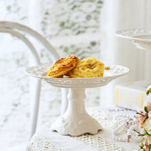 Load image into Gallery viewer, Juliette White Lace Dinnerware by Allthingscurated adds an elegant touch to your tabletop. This sophisticated set is crafted out of ceramic with a beautiful embossed lace rim, giving it a vintage touch. The creamy white pieces come in a dinner plate and cake stand in 2 sizes for easy mixing and matching. They are perfectly sized for a main course, starters and desserts.