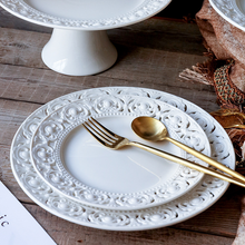 Load image into Gallery viewer, Juliette White Lace Dinnerware by Allthingscurated adds an elegant touch to your tabletop. This sophisticated set is crafted out of ceramic with a beautiful embossed lace rim, giving it a vintage touch. The creamy white pieces come in a dinner plate and cake stand in 2 sizes for easy mixing and matching. They are perfectly sized for a main course, starters and desserts.