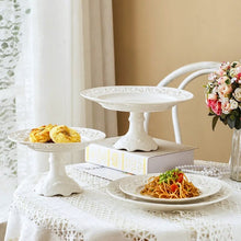 Load image into Gallery viewer, Juliette White Lace Dinnerware by Allthingscurated adds an elegant touch to your tabletop. This sophisticated set is crafted out of ceramic with a beautiful embossed lace rim, giving it a vintage touch. The creamy white pieces come in a dinner plate and cake stand in 2 sizes for easy mixing and matching. They are perfectly sized for a main course, starters and desserts.