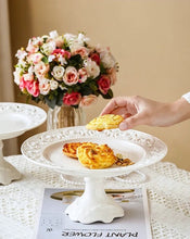 Load image into Gallery viewer, Juliette White Lace Dinnerware by Allthingscurated adds an elegant touch to your tabletop. This sophisticated set is crafted out of ceramic with a beautiful embossed lace rim, giving it a vintage touch. The creamy white pieces come in a dinner plate and cake stand in 2 sizes for easy mixing and matching. They are perfectly sized for a main course, starters and desserts.