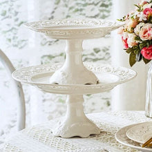 Load image into Gallery viewer, Juliette White Lace Dinnerware by Allthingscurated adds an elegant touch to your tabletop. This sophisticated set is crafted out of ceramic with a beautiful embossed lace rim, giving it a vintage touch. The creamy white pieces come in a dinner plate and cake stand in 2 sizes for easy mixing and matching. They are perfectly sized for a main course, starters and desserts.
