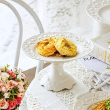 Load image into Gallery viewer, Juliette White Lace Dinnerware by Allthingscurated adds an elegant touch to your tabletop. This sophisticated set is crafted out of ceramic with a beautiful embossed lace rim, giving it a vintage touch. The creamy white pieces come in a dinner plate and cake stand in 2 sizes for easy mixing and matching. They are perfectly sized for a main course, starters and desserts.