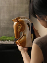 Load image into Gallery viewer, Person holding a ceramic horse sculpture indoors. Jyunma Ceramic Horse by Allthingscurated is handmade artistry at its finest. It’s more than just decoration, it embodies auspiciousness and prosperity; represents steadfast loyalty and protective guardianship through time. Its elegance makes it a perfect gift for any horse enthusiasts or anyone born under the Chinese zodiac sign of the horse; and an exquisite addition to any contemporary home for its enduring appeal.