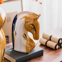 Load image into Gallery viewer, Decorative horse head sculpture on a book with a blurred background. Jyunma Ceramic Horse by Allthingscurated is handmade artistry at its finest. It’s more than just decoration, it embodies auspiciousness and prosperity; represents steadfast loyalty and protective guardianship through time. Its elegance makes it a perfect gift for any horse enthusiasts or anyone born under the Chinese zodiac sign of the horse; and an exquisite addition to any contemporary home for its enduring appeal.