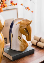 Load image into Gallery viewer, Decorative horse head sculpture on a book with a blurred background. Jyunma Ceramic Horse by Allthingscurated is handmade artistry at its finest. It’s more than just decoration, it embodies auspiciousness and prosperity; represents steadfast loyalty and protective guardianship through time. Its elegance makes it a perfect gift for any horse enthusiasts or anyone born under the Chinese zodiac sign of the horse; and an exquisite addition to any contemporary home for its enduring appeal.