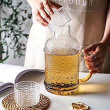 Load image into Gallery viewer, Kiv Hammered Glass Pitcher with Cover in 2 liter or 68 ounce capacity by Allthingscurated. Comes with a hemp rope handle for a rustic vibe. Large capacity and heat-resistant. It's the perfect thirst quencher for summer.