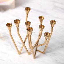 Load image into Gallery viewer, Lysa Gold Candelabra by Allthingscurated spots an asymmetrical design and clean lines that exude modern elegance. With 9 arms for taper candles, the gold-tone metal surface reflects the glow of the flames, creating a warm and captivating atmosphere. It’s stunning centerpiece for any occasion and decorative accent for any event or space.