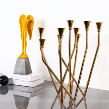 Load image into Gallery viewer, Lysa Gold Candelabra by Allthingscurated spots an asymmetrical design and clean lines that exude modern elegance. With 9 arms for taper candles, the gold-tone metal surface reflects the glow of the flames, creating a warm and captivating atmosphere. It’s stunning centerpiece for any occasion and decorative accent for any event or space.