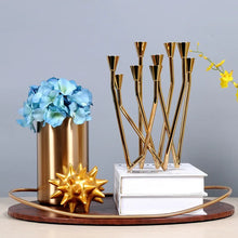 Load image into Gallery viewer, Lysa Gold Candelabra by Allthingscurated spots an asymmetrical design and clean lines that exude modern elegance. With 9 arms for taper candles, the gold-tone metal surface reflects the glow of the flames, creating a warm and captivating atmosphere. It’s stunning centerpiece for any occasion and decorative accent for any event or space.