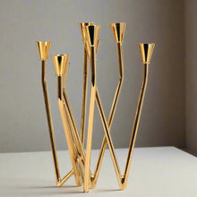 Load image into Gallery viewer, Lysa Gold Candelabra by Allthingscurated spots an asymmetrical design and clean lines that exude modern elegance. With 9 arms for taper candles, the gold-tone metal surface reflects the glow of the flames, creating a warm and captivating atmosphere. It’s stunning centerpiece for any occasion and decorative accent for any event or space.