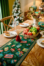 Load image into Gallery viewer, Dining table set with a festive table runner, fruit basket, and Christmas tree in the background. Elevate your holiday entertaining with this Merry Christmas Jacquard Table Runner by Allthingscurated. Inspired by the joy of gift-giving, this table runner features an array of gift box motifs rendered in rich jewel tones, this piece showcases beautiful embroidery complemented by pretty tassels. Perfect for elevating your holiday tablescape, making every feast and gathering truly memorable.