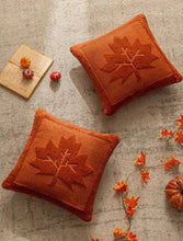 Load image into Gallery viewer, Two orange pillows with maple leaf patterns on a textured surface with decorative items. The Velour Maple Leaf Cushion Cover by Allthingscurated is a beautiful way to bring the warmth of fall into your home. With its elegant tufted pumpkin design and soft velour fabric, it offers both comfort and style. Perfect for autumn and Thanksgiving, this decorative pillow adds a cozy, inviting touch to any space.