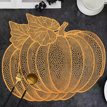 Load image into Gallery viewer, A pumpkin-shaped placemat with an intricate openwork web-like pattern in orange, styled on a dark textured tabletop with gold-toned cutlery and a white cup in the background. Pumpkin Vinyl Placemats by Allthingscurated are designed with perforated hollow patterns to create a unique texture and add dimension to your table setting. Made from durable PVC vinyl, they are stain-resistant and easy to maintain. Perfect for Thanksgiving and Halloween celebrations.