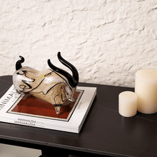 Load image into Gallery viewer, Glass bull figurine on books with candles on a table against a textured wall. Rex Decorative Bull by Allthingscurated are meticulously handmade from high quality glass. Comes in three striking finishes—an all-all black edition or two-tone variants featuring bold graphic elements. Rex brings contemporary flair and bold energy to any room. More than décor, it’s an ideal gift for those born under the Ox zodiac and Taurus sign.