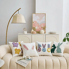 Load image into Gallery viewer, Decorative pillows with colorful bunny and butterfly designs on a beige sofa in a living room setting. Spring Melody Embroidered Cushion Covers by Allthingscurated feature charming seasonal details to transition your home into Spring and Easter effortlessly. Each cover showcases meticulous embroidery to add depth and visual interest to your sofa and furniture.