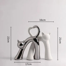 Load image into Gallery viewer, These Cat Couple Love Figurines by Allthingscurated are perfect for cat lovers. Made of ceramic, they feature a pair of cute and whimsical cats in contrasting colors, with their tails entwined to form a heart shape. A romantic and unique gift for any occasion.  This set features a pair of silver and white cats.