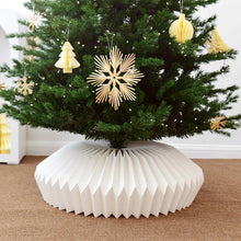 Load image into Gallery viewer, Decorative Christmas tree with a white paper base and gold ornaments. Transform your holiday setup with the striking Honeycomb Christmas Tree Collar by Allthingscurated. Crafted from premium paper with easy setup, its distinctive pleated design delivers sophisticated visual interest while concealing the tree base with understated elegance. The crips white finish works beautifully with any tree style.