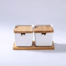 Load image into Gallery viewer, Ceramic Seasoning Storage Jars by Allthingscurated are the perfect storage solution to keep your herbs, seasonings and spices. Made of durable ceramic with a sustainable bamboo flip lid for easy access during cooking. These jars are not only functional but also environmentally friendly. Comes with a bamboo tray and ceramic spoons. Featured here is a set of 2 white jars with spoons and tray.