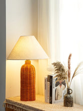 Load image into Gallery viewer, Decorative rattan lamp on a table with books and a vase in a softly lit room. The Yumi Japanese Table Lamp by Allthingscurated embraces the wabi-sabi philosophy that profound beauty emerges from simplicity. Crafted from natural rattan, its minimalist design feels both rustic and contemporary. It elevates your home décor by transforming any space into a sanctuary of quiet sophistication.