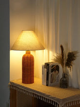 Load image into Gallery viewer, Rattan lamp on a side table with a curtain in the background. The Yumi Japanese Table Lamp by Allthingscurated embraces the wabi-sabi philosophy that profound beauty emerges from simplicity. Crafted from natural rattan, its minimalist design feels both rustic and contemporary. It elevates your home décor by transforming any space into a sanctuary of quiet sophistication.