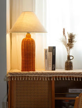 Load image into Gallery viewer, Rattan lamp on a side table with books and a vase. The Yumi Japanese Table Lamp by Allthingscurated embraces the wabi-sabi philosophy that profound beauty emerges from simplicity. Crafted from natural rattan, its minimalist design feels both rustic and contemporary. It elevates your home décor by transforming any space into a sanctuary of quiet sophistication.