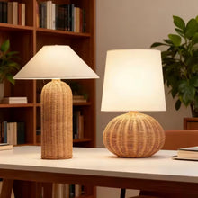 Load image into Gallery viewer, Two rattan table lamps on a desk with a bookshelf and plant in the background. The Yumi Japanese Table Lamp by Allthingscurated embraces the wabi-sabi philosophy that profound beauty emerges from simplicity. Crafted from natural rattan, its minimalist design feels both rustic and contemporary. It elevates your home décor by transforming any space into a sanctuary of quiet sophistication.