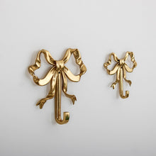 Load image into Gallery viewer, These pretty wall hooks by Allthingscurated are made of high-quality brass with a vintage gold finish.  Fashioned like a bow tied with ribbon, it’s feminine and perfect for the walk-in wardrobe or powder room. Comes in small and large size. Small hook measures 7.3cm or 2.8 inches in height and 6.5cm or 2.5 inches in width. Large hook measures 10.3cm or 4 inches in height and 9.5cm or 3.7 inches in width. Sold as individual hooks or a set of small and large hooks.