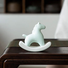 Load image into Gallery viewer, This Petite Ceramic Rocking Horse by Allthingscurated is a work of art. Crafted by hand from ceramic and decorated with a beautiful crackle pattern, it exudes a subtle far-eastern beauty and grace. Makes a perfect gift for those who appreciate quality craftsmanship and a treasured gift to any horse collector. Comes in green and azurerish white. Measures 9.8cm or 3.8 inches in height, 10.4cm or 4 inches in width and 4.2cm or 1.6 inches in depth. Featured here is an Azurerish White horse.
