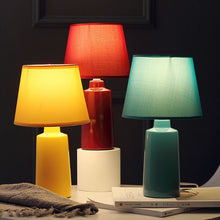 Load image into Gallery viewer, Burano Table Lamp by Allthingsucrated comes in 3 gorgeous colors in Red, Blue and Yellow.  The lamp base is made of ceramic and the lampshade of fabric.  Both the base and lampshade are of the same color.  Featured here are 3 lamps with light being switched on.
