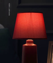 Load image into Gallery viewer, Burano Table Lamp by Allthingsucrated comes in 3 gorgeous colors in Red, Blue and Yellow.  The lamp base is made of ceramic and the lampshade of fabric.  Both the base and lampshade are of the same color.  Featured here is the red lamp with light being switched on.
