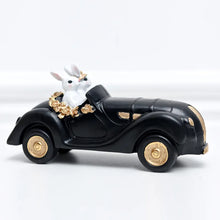 Load image into Gallery viewer, Our Regal Rabbit Family Figurines by Allthingscurated are beautifully-crafted and decorative. Made high-quality resin, these unique figurines will add a touch of elegance and whimsy to your home décor. Available in 6 designs, they are the perfect additions to your spring and Easter decorations. Featured here is Car Riding Rabbits.

